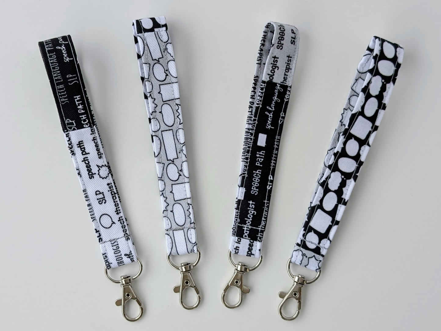 Four black and white patterned lanyards with metal hooks on a light gray background