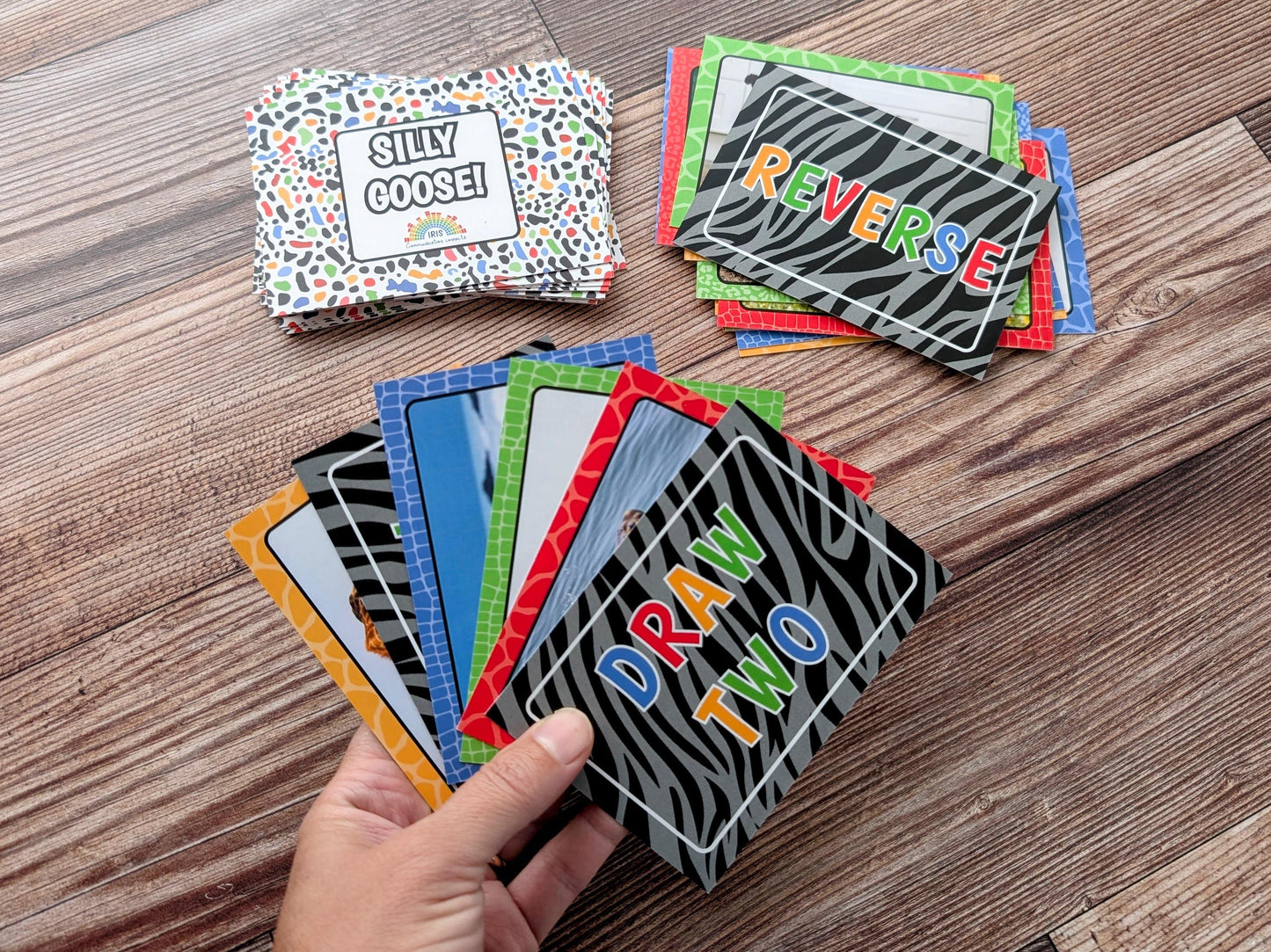 Colorful card game cards on a wooden surface with a hand holding some of the cards.