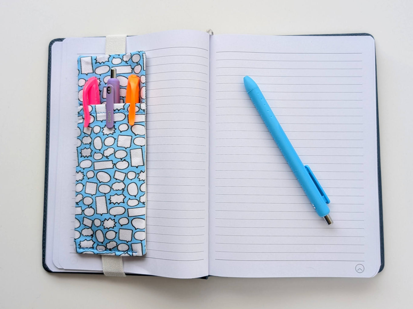 Open notebook with colorful markers and a blue pen on a light background