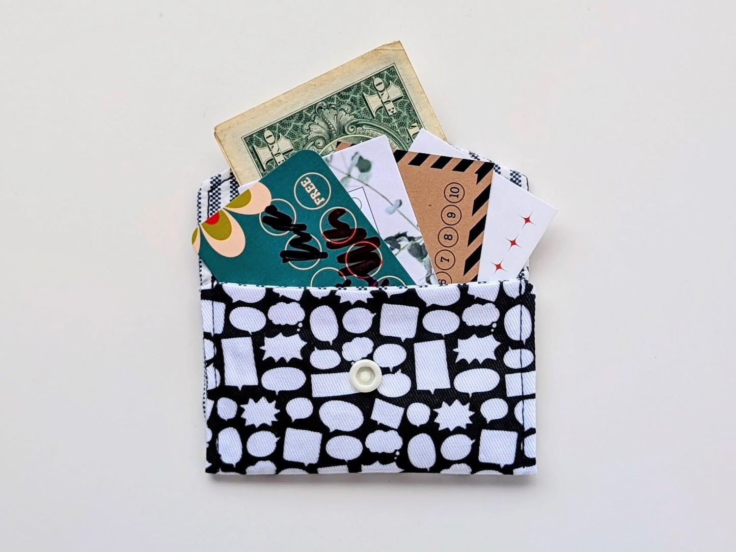 Black and white patterned wallet with cards and money on a light gray background