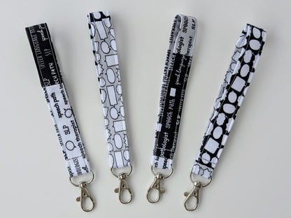 Four black and white patterned lanyards with metal hooks on a light gray background