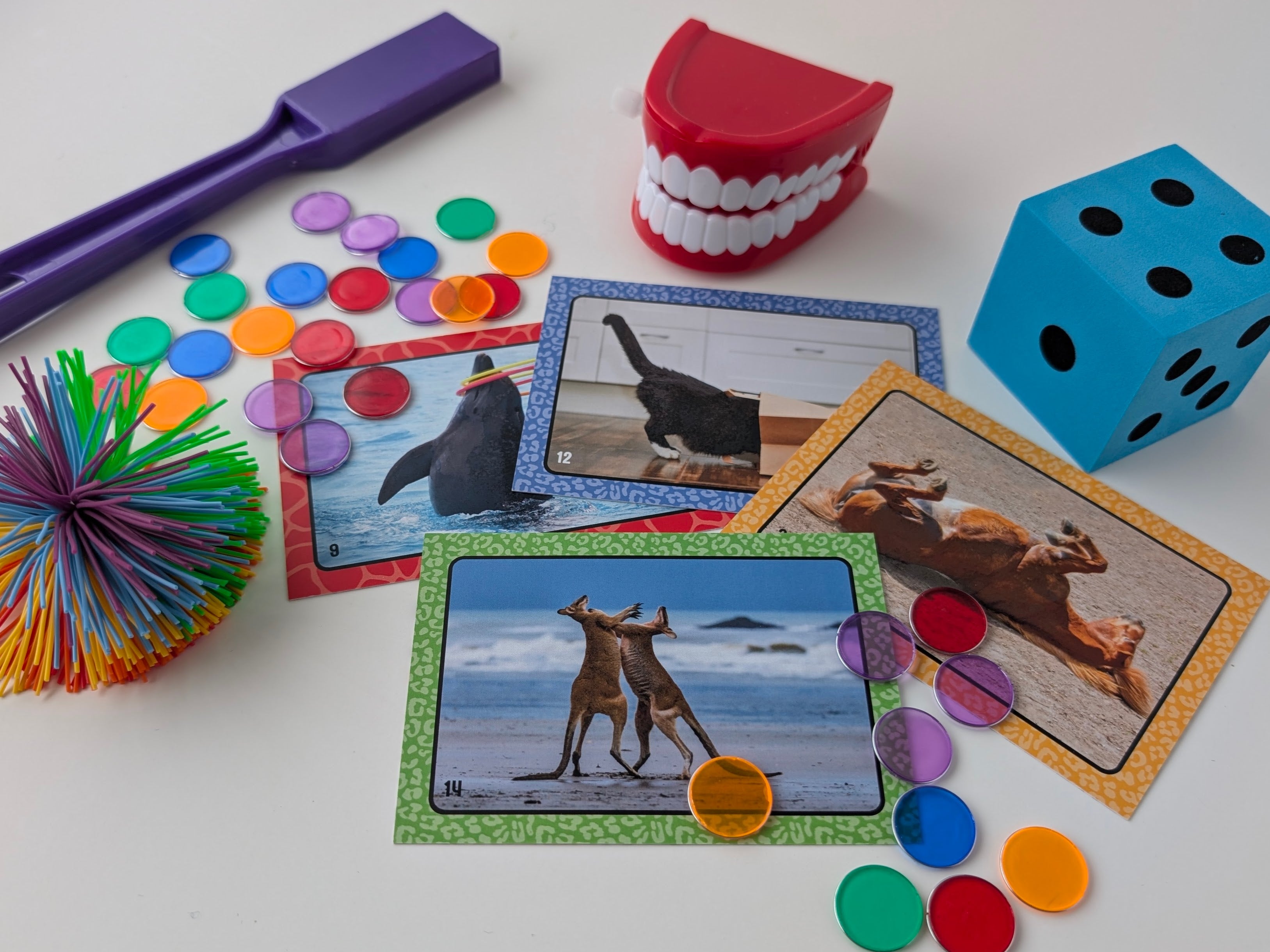 Educational game with cards, dice, and colorful objects on a white surface