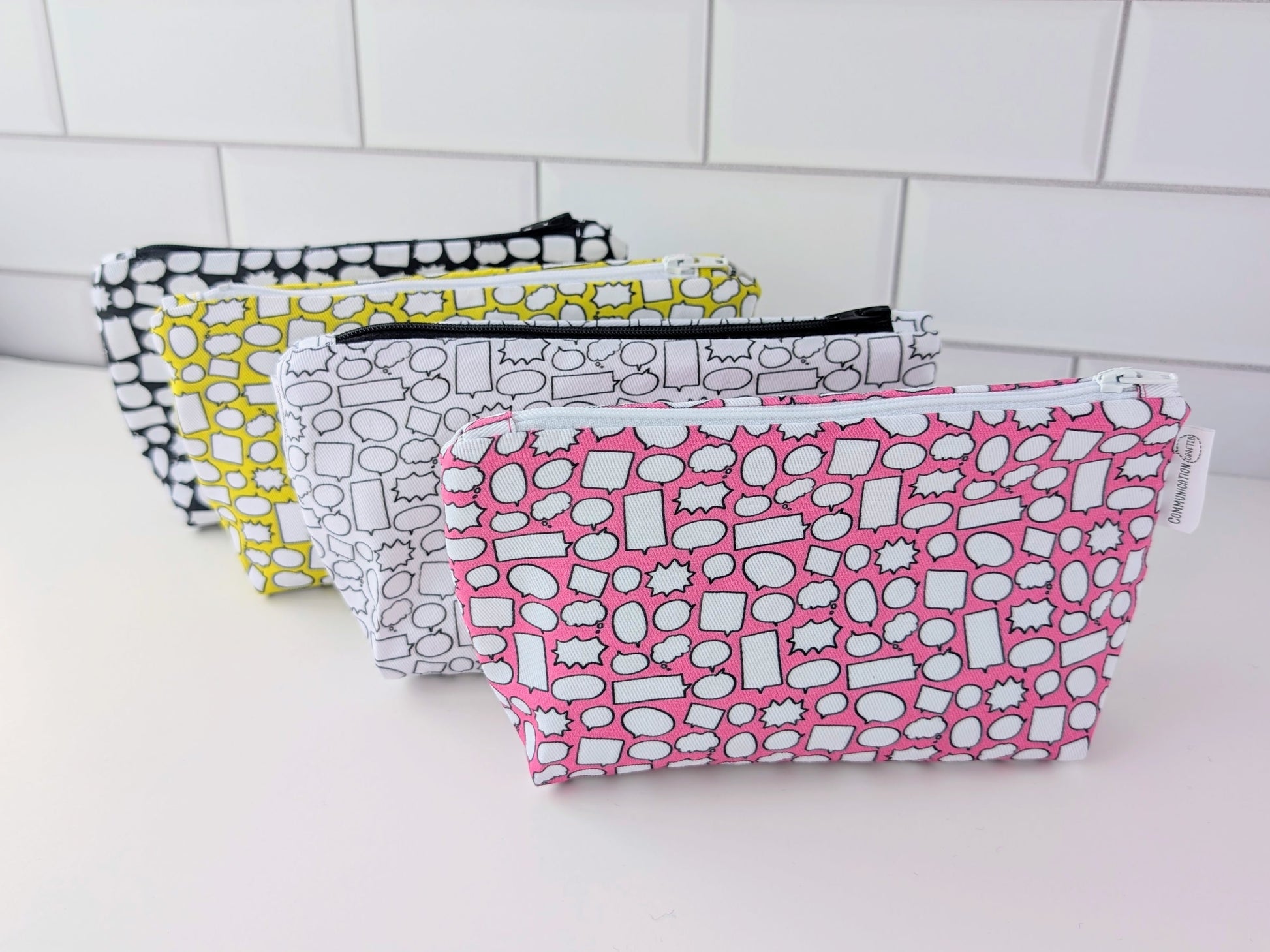 Four patterned pouches on a white surface with a tiled wall background