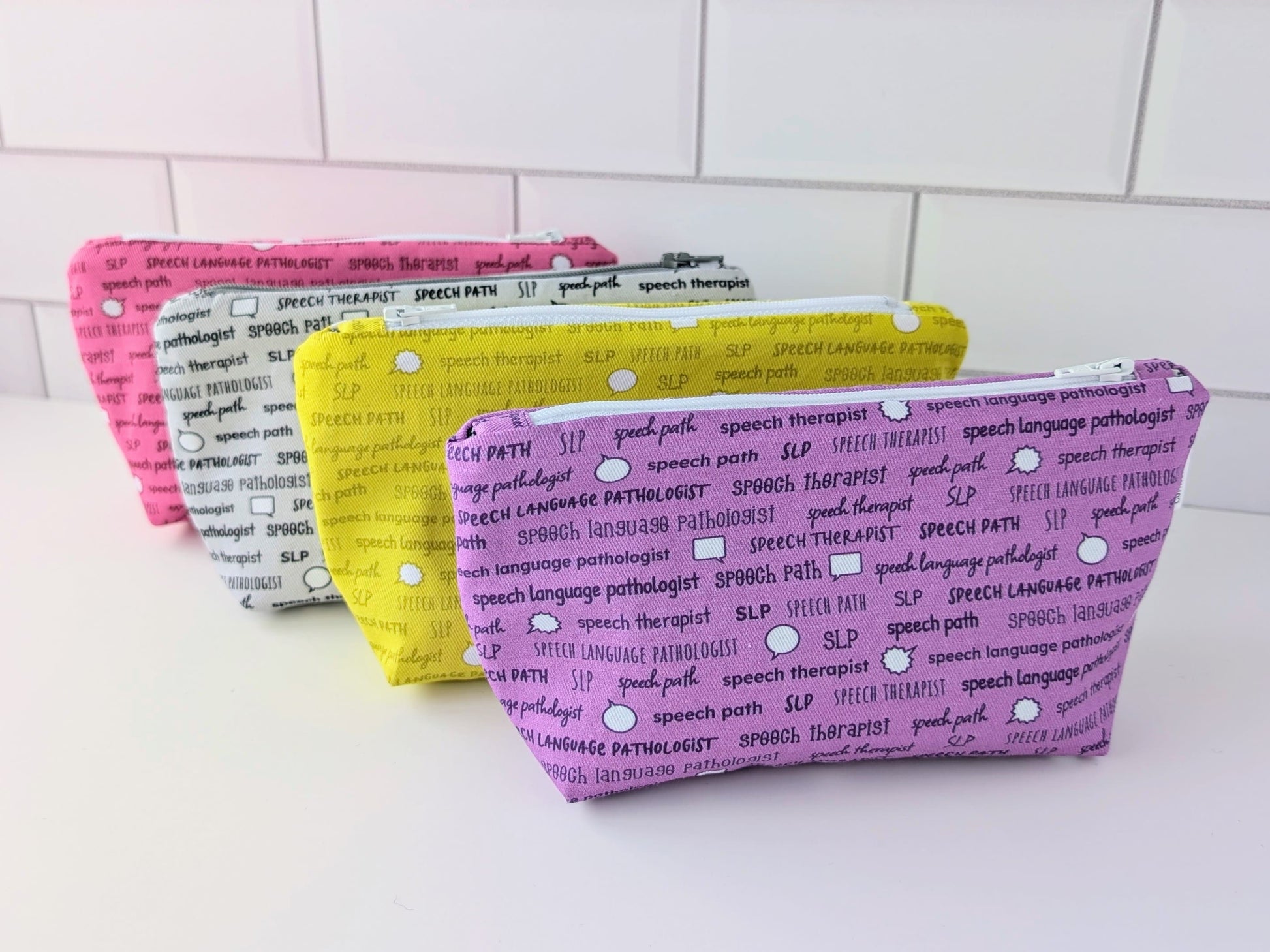 Four pouches with text patterns on a white surface and tiled wall background